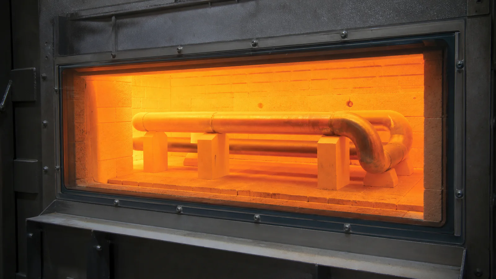 Supported U-shaped stainless radiant tube operating behind a closed glowing furnace shield